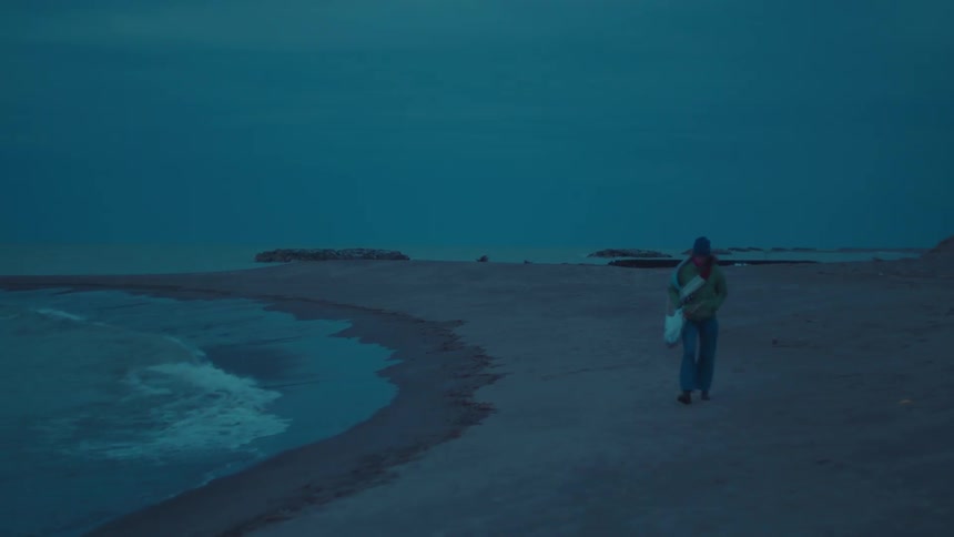 Woman carrying a bag as she walks on the beach and waves roll in to shore