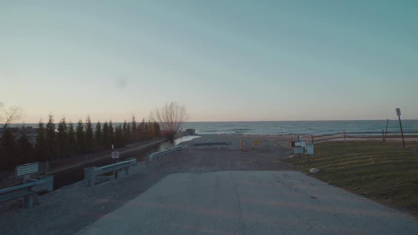 A quiet concrete road leads to a coastal waterfront at sunset