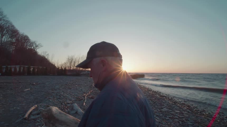 Man in cap holding a branch while standing on a beach in winter
