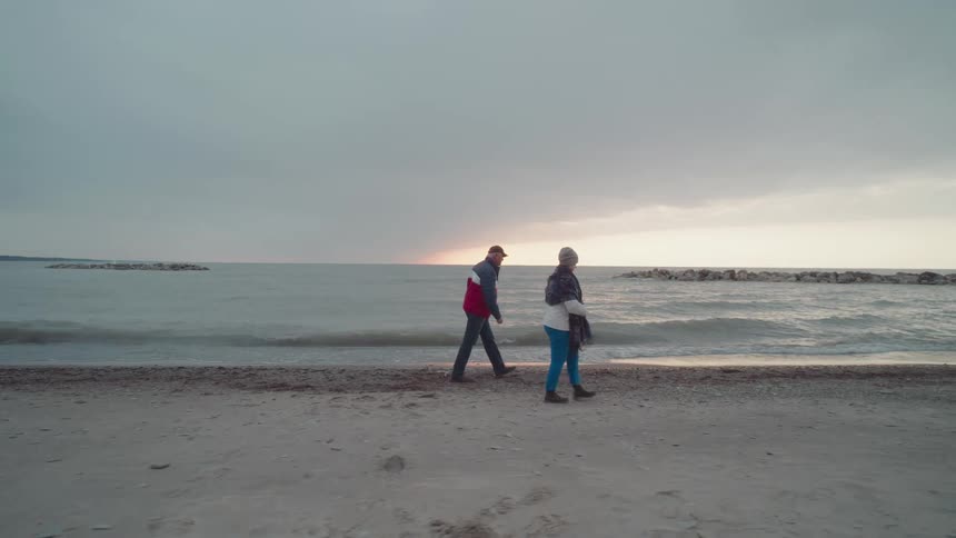 Two people walk along a quiet beach at sunset