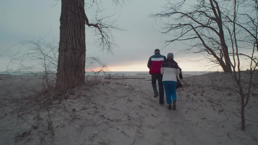 A man and woman hold hands while walking on the beach