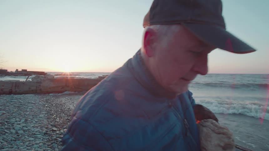 A man carries logs along a rocky beach next to the ocean