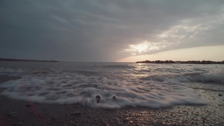 Waves gently wash over a rocky shore under a dramatic sunset sky