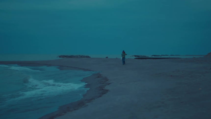 A man walks along the shoreline in the evening as ocean waves hit the beach