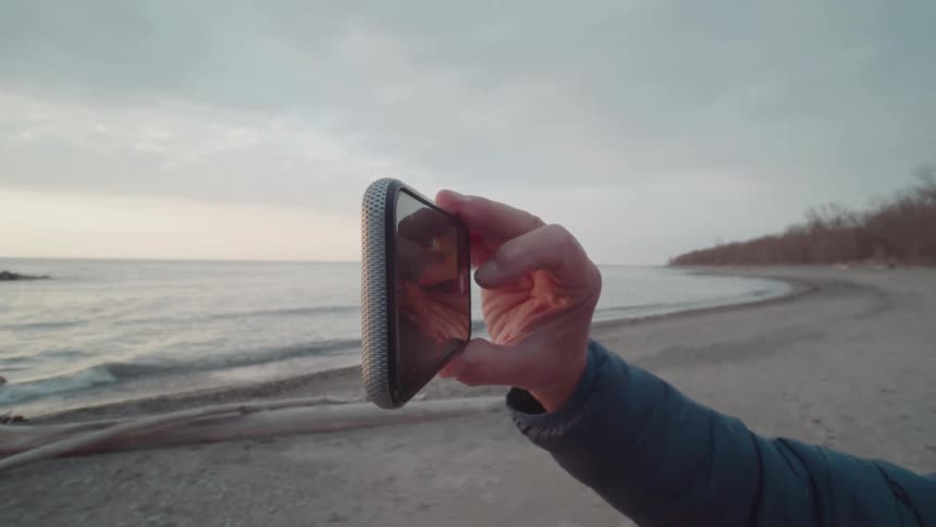 Man taking a picture of the horizon on a beach at dawn with a smartphone