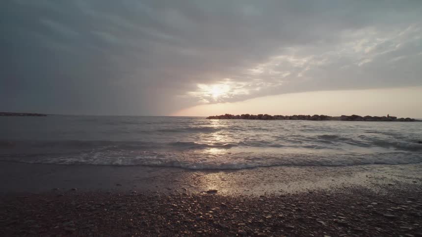 Waves gently roll onto a rocky beach under a moody sky at sunset