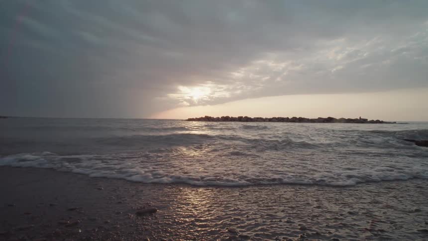 The sun sets over the ocean casting a golden reflection on the water as gentle waves wash over a pebbly shore