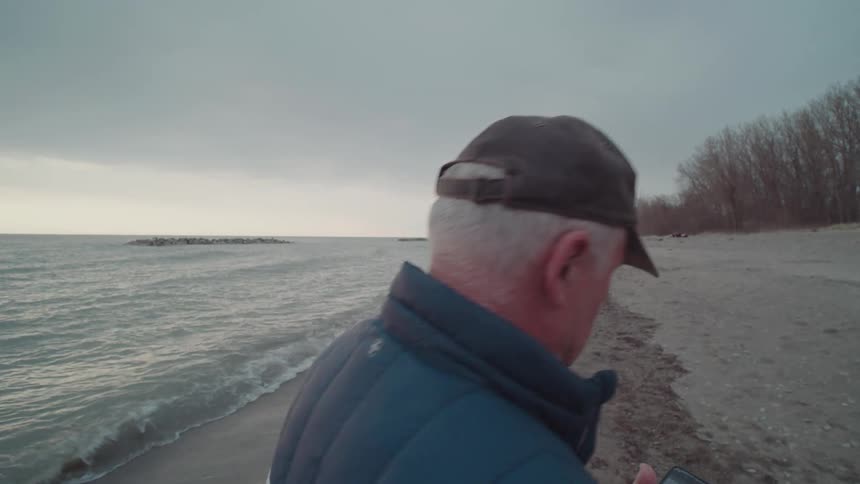 Man holding a smartphone and walking on a beach in winter