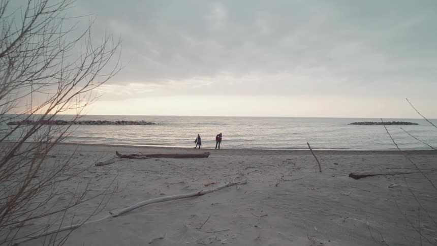 Two people walk along the coast on the beach as waves roll in to shore