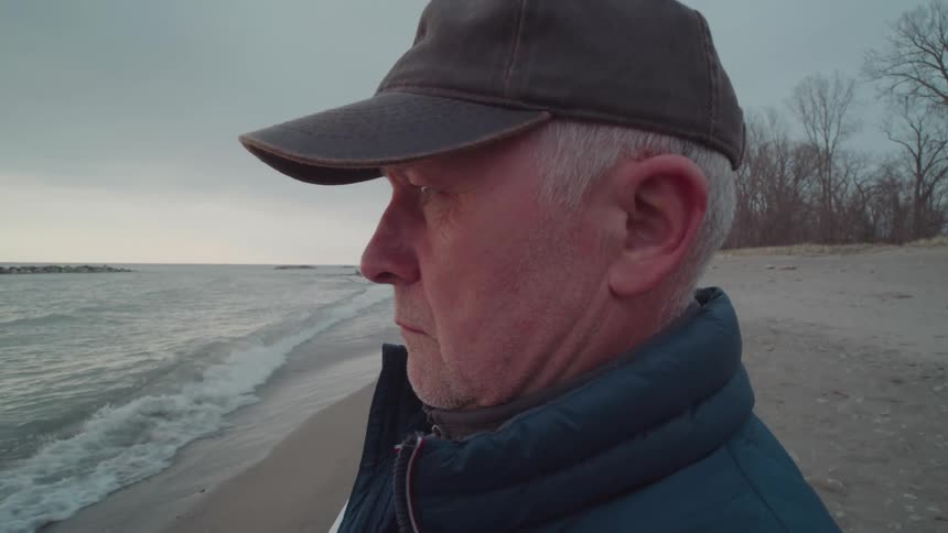 An older man takes a photo of the ocean at the beach with his smartphone