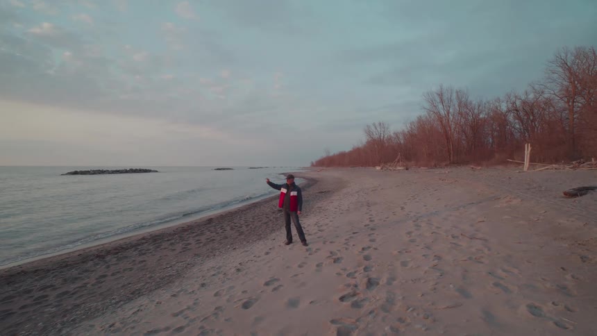 A man walks on the beach around midday wearing a jacket as waves from the ocean hit the shore