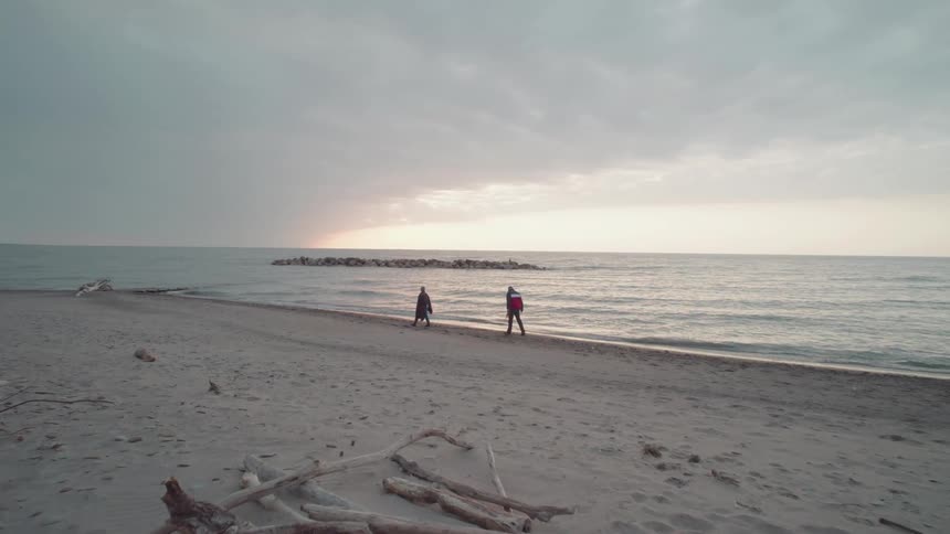 Two people walking on a deserted beach on a cloudy morning