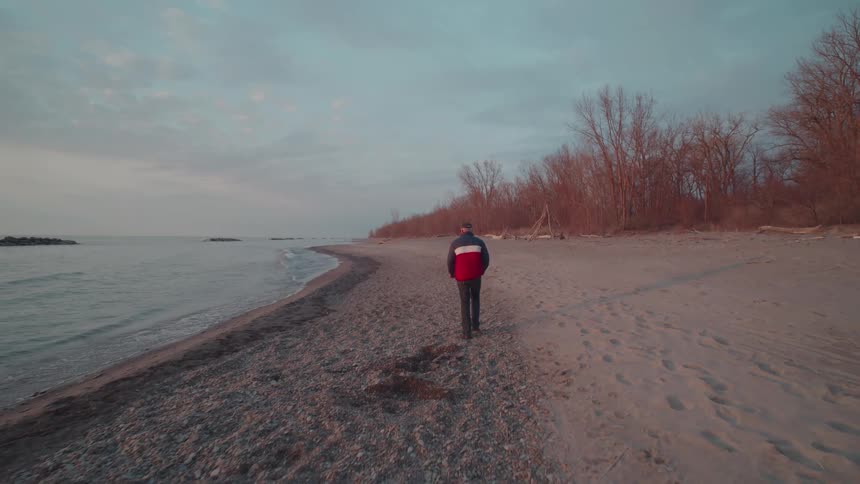 A person walks alone along a quiet beach at sunset