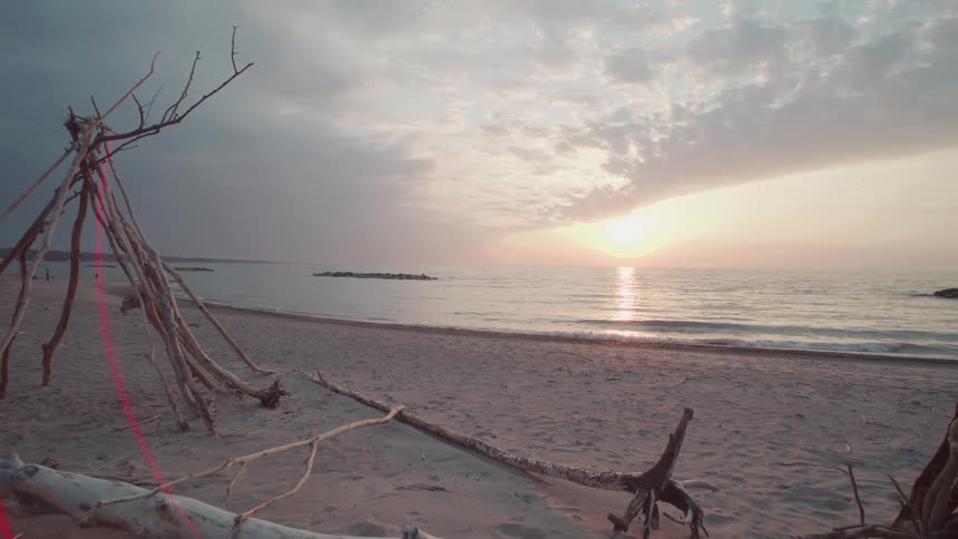 A serene beach at sunset with driftwood structures scattered across the sand