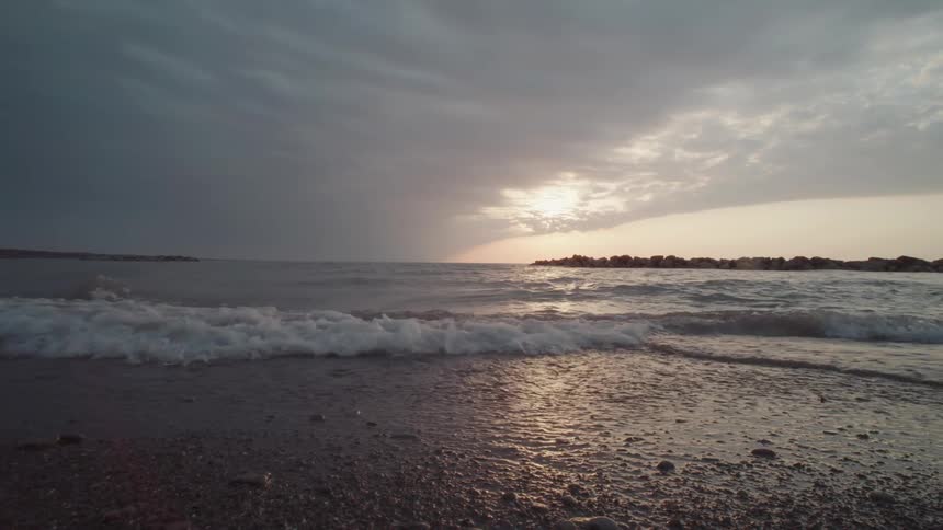 Waves gently wash over a pebbled beach at sunset under a dramatic sky
