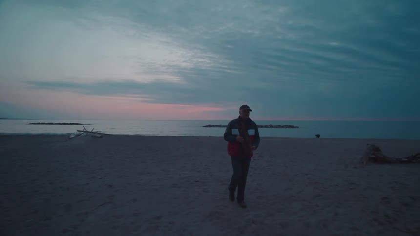 Man carrying a piece of driftwood as he walks across the beach