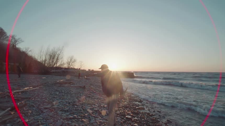 Man walking on rocks by the sea picking up pieces of wood at sunrise