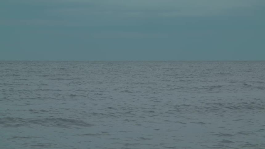 Calm ocean waves ripple under a soft blue sky