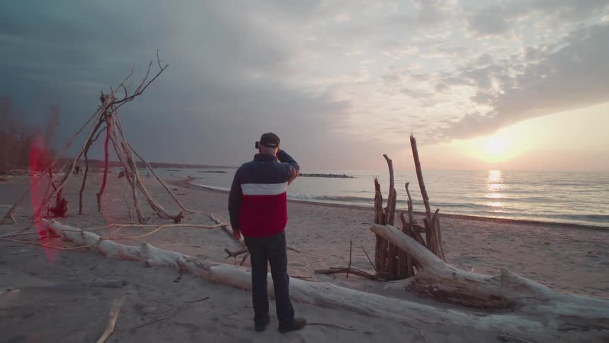 A person stands on a beach photographing the ocean at sunset