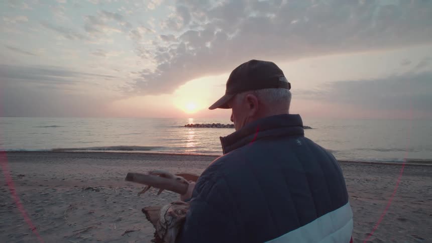 Man stands on the beach looking at pieces of driftwood in his hands