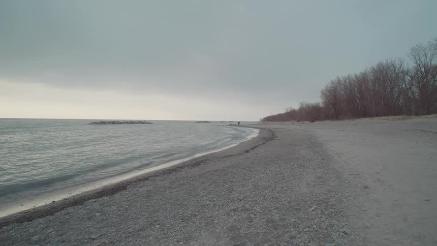 A quiet empty beach stretches along the shoreline under a cloudy sky