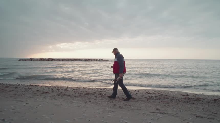Man in cap walking on the beach in the morning and picking up twigs