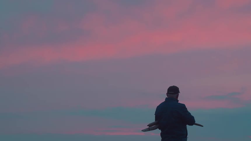 Man in cap holding branches in open air environment with pink sky
