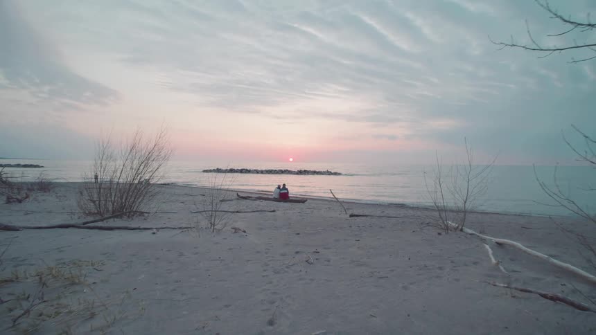 Two people sit on driftwood on the beach