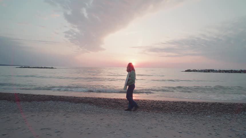 A woman walks alone along a beach at sunset