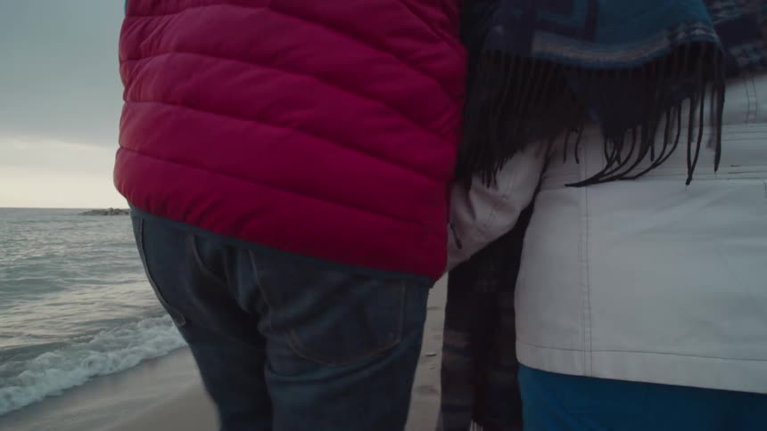 Older couple holding hands walking along the shoreline at sunrise in the winter