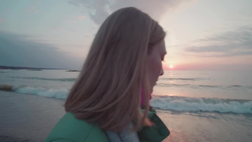 The woman is walking on the beach at sunrise