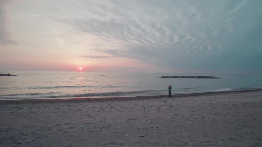A person stand along a quiet beach at sunset beside a wooden teepee like structure