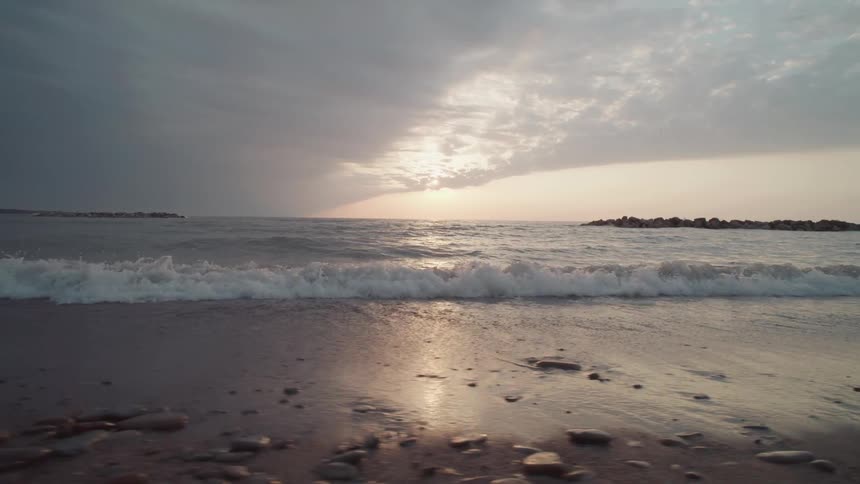 Waves gently wash over a rocky beach under a dramatic cloud streaked sunset