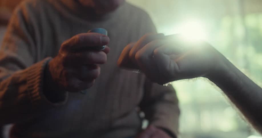 Hand of an elderly person being helped by another person who is holding a remote control