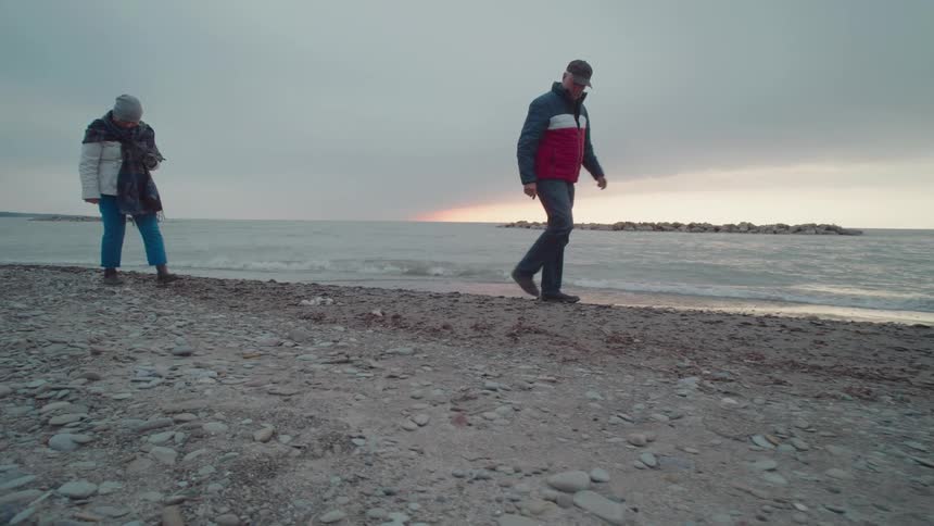 Two people walk quietly along a rocky beach at sunset