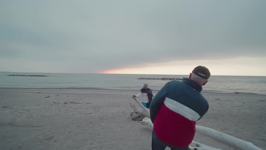 Person poses on beach while another takes photo at sunset