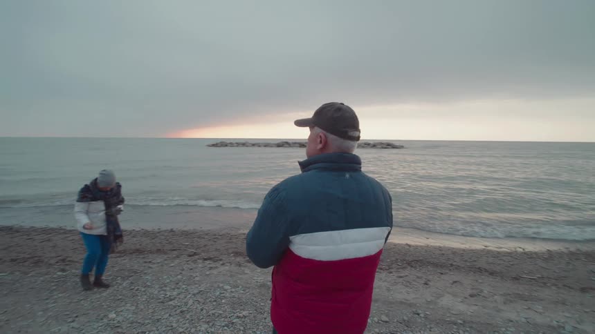 Man with a woman walking on the beach with the man filming with a smartphone