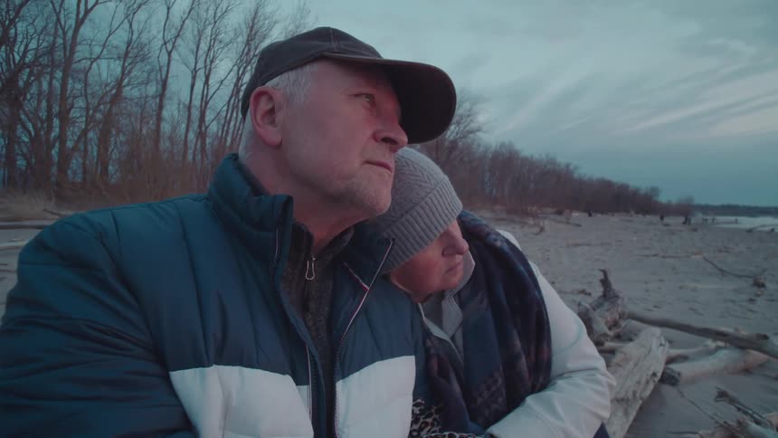 Couple hugging sitting on a log on a beach in winter