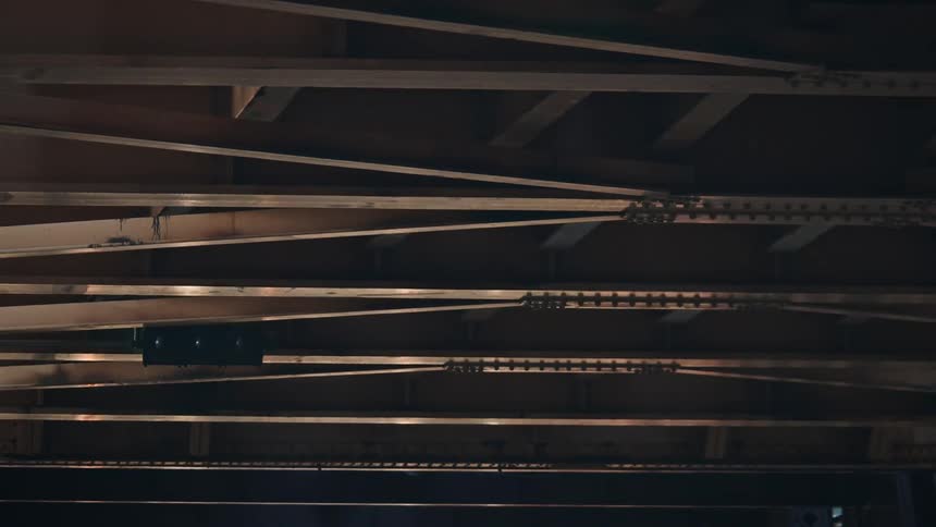Headlights from traffic reflect off the underside of a metal covered bridge.