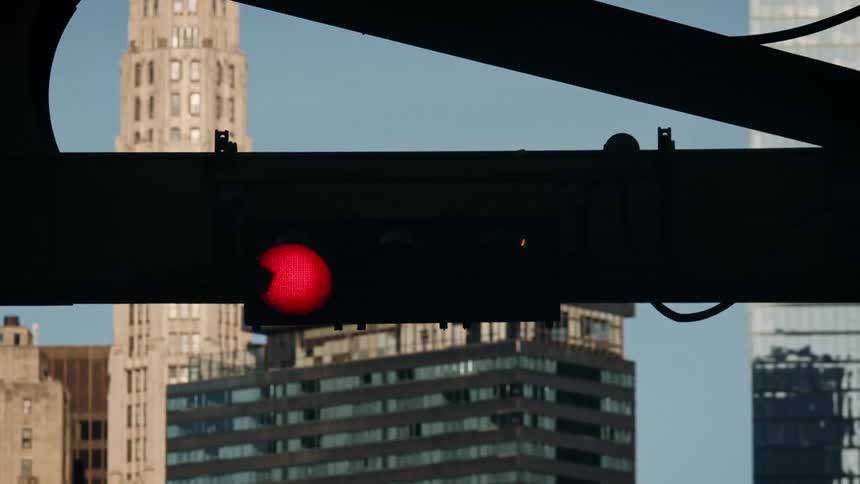 Traffic light quickly cycles through its colours with a downtown skyline backdrop