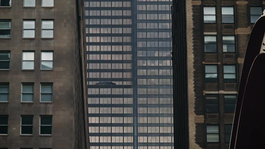 A timelapse shows clouds speeding by in the reflections of the glass windows of tightly packed city skyscrapers