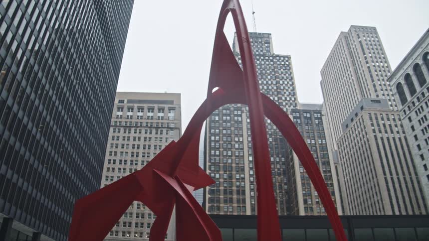 A person walks past an abstract monument surrounded by skyscrapers in a metropolis