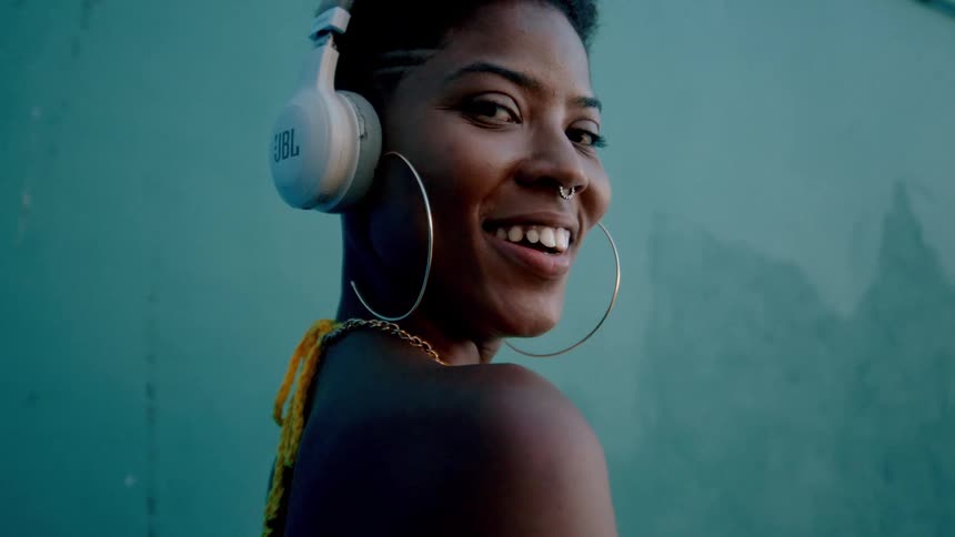 A stylish woman smiles while modeling with headphones against a bold teal wall