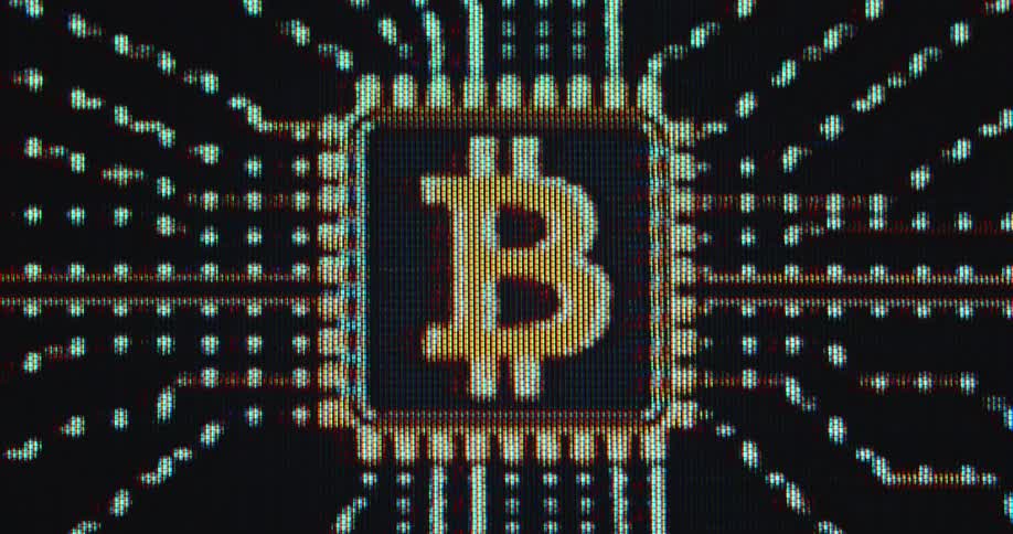 A glowing orange bitcoin symbol sits on a digital microchip of a computer system or mainboard symbolizing crypto computing power in a decentralised network while mining blocks of the crypto currency and validating transactions