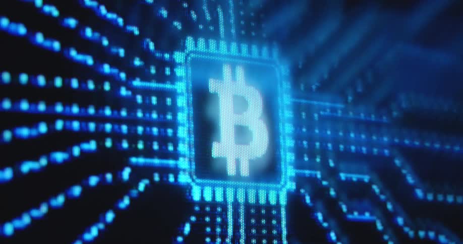 Pixelated white bitcoin logo glows on a computer chip while a block of BTC is being mined by a mining company running server farms supporting the decentralised network of the cryptocurrency while investing in the digital revolution