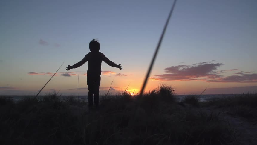 The silhouette of a child raising his arms while standing overlooking the sun rise over the ocean