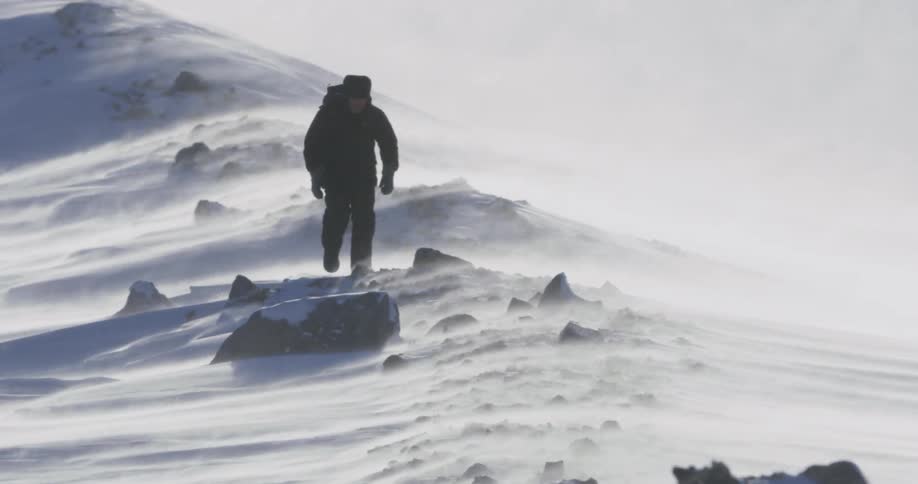 A man is hiking along the rocks in the snow