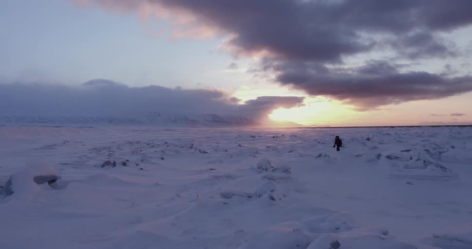 A person is hiking along the shore at sunset