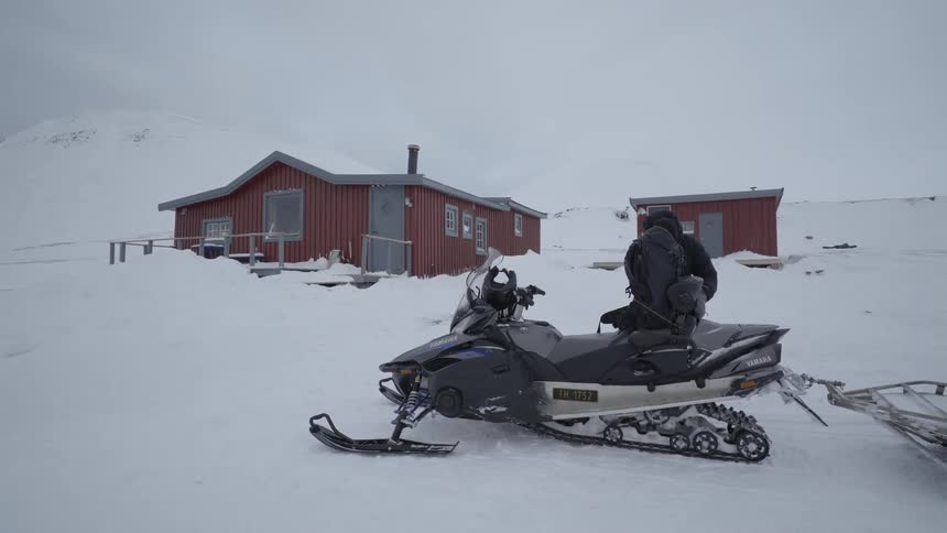 Man leaving building surrounded by snow and driving off on snowmobile