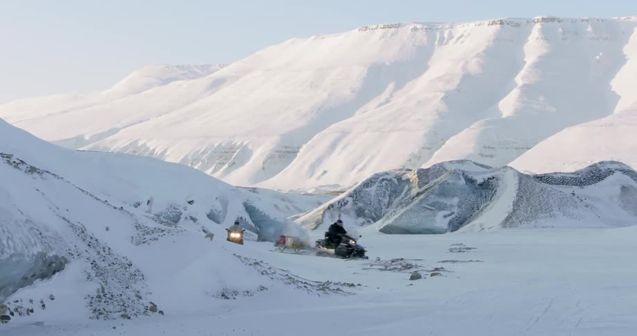 A snowmobile turns a corner around a snow covered mountain